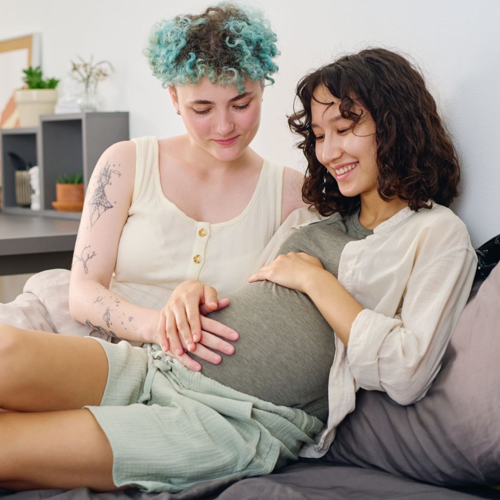 Two BIPOC women sit on a couch, smiling and engaging in conversation during a LGBTQ+ training session.