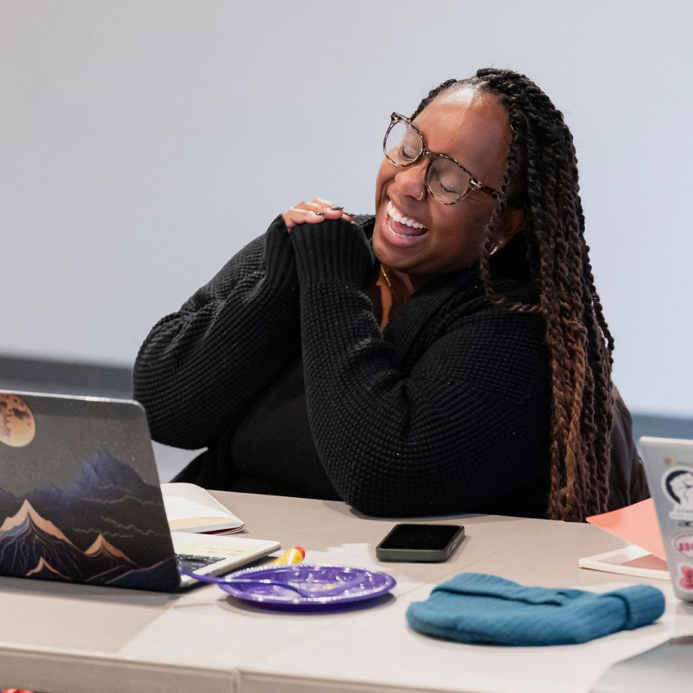 A woman at a table with a laptop and coffee, focused on her In-Person Doula Training session.